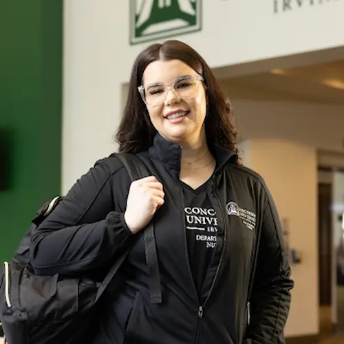A woman with glasses, smiling and holding a backpack